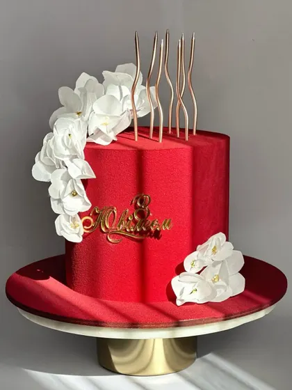 A striking red velvet-textured cake with a cascade of white sugar flowers and modern, wavy candles. This design is bold and beautiful.