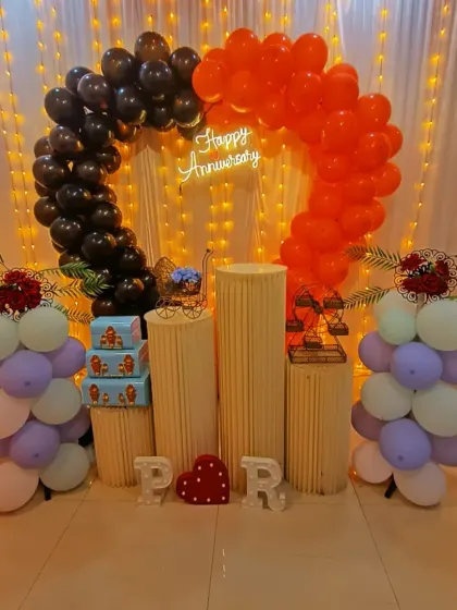 An anniversary decoration with a unique half-and-half balloon arch in black and orange. The light-up initials "P" and "R" add a personalized touch for the couple.