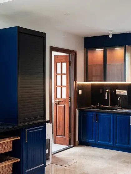 Another view of the bold blue kitchen, showing the integrated tall unit with a black rolling shutter and a decorative floral wallpaper accent wall.