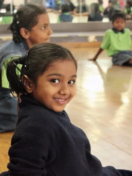 A student from our outreach program smiles over her shoulder. We aim to create a space where every child feels seen, valued, and happy.