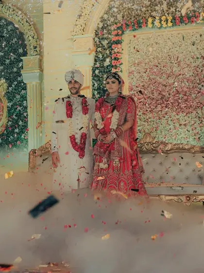 A grand, wide shot of the couple on stage, showered with confetti. The smoke and falling petals create a magical, dream-like atmosphere for their wedding portrait.