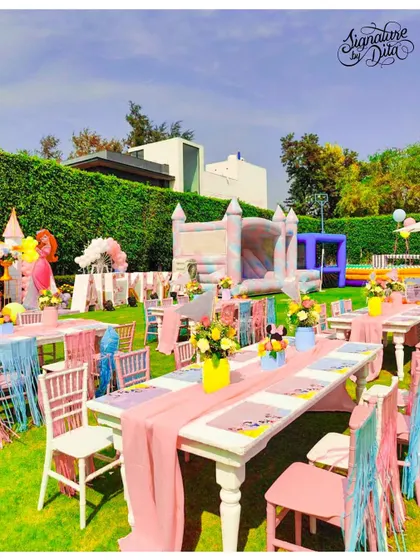 An overview of the kids' dining area at the Disneyland party. The long tables are decorated with pastel pink runners and fringed chair details, with a large bouncy castle visible in the background for fun.