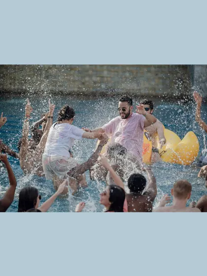 The pool party is in full swing as guests lift the groom and splash around in the water.