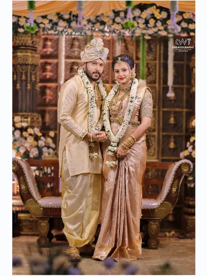 A full-length formal portrait of a couple in matching cream-colored traditional outfits, a classic shot for any wedding album.