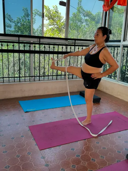 A student practices Utthita Hasta Padangusthasana (Extended Hand-to-Big-Toe Pose) with a strap. This modification allows for a full hamstring stretch without compromising the alignment of the spine and hips.