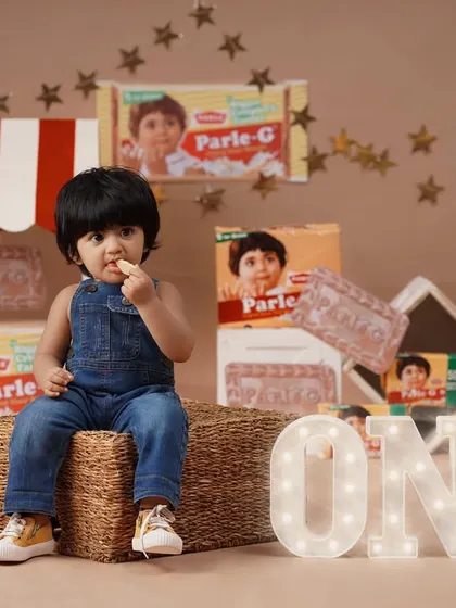 The Parle-G theme is combined with a first birthday milestone, featuring a light-up 'ONE' sign next to the baby girl.