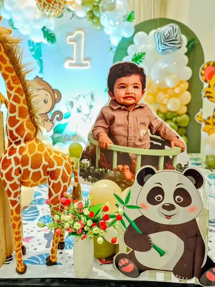 A personalized cutout of the birthday boy, Atharva, placed amongst his favorite jungle animals like a giraffe and panda for his 'Wild One' party.