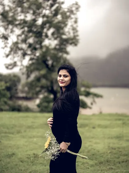 A lovely portrait of the mom-to-be looking at the camera, holding a single sunflower. The lakeside setting and her gentle smile create a peaceful and beautiful image.