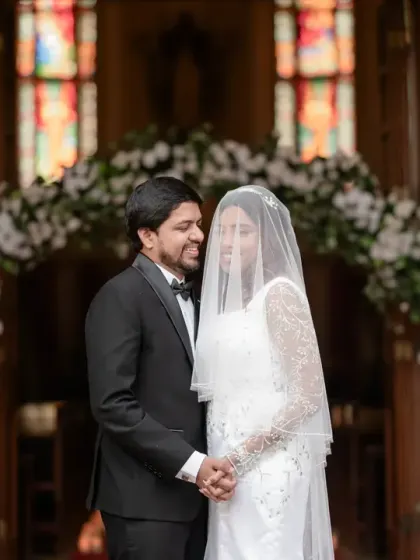 The couple stands under the floral arch at the church entrance, sharing a quiet moment after their vows. The stained glass window in the background adds a touch of timeless beauty.