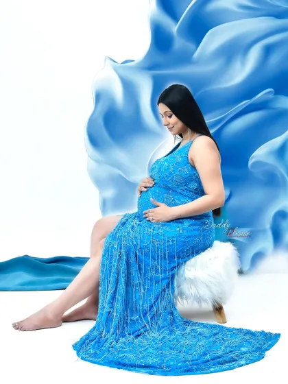 A serene portrait of a mom-to-be in a sparkling blue gown. The flowing blue fabric in the background adds a touch of magic and movement to this beautiful studio shot.