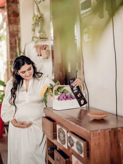 The mom-to-be arranges her sonogram and flowers on a wooden dresser, a quiet moment of nesting and preparation.