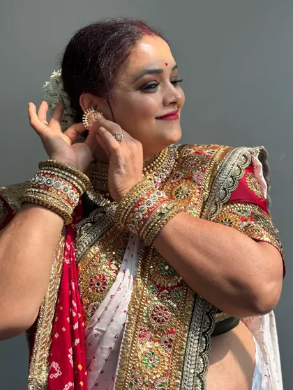 A candid shot of the bride adjusting her earring. Her makeup is classic and elegant, with a red lip that ties the whole look together.