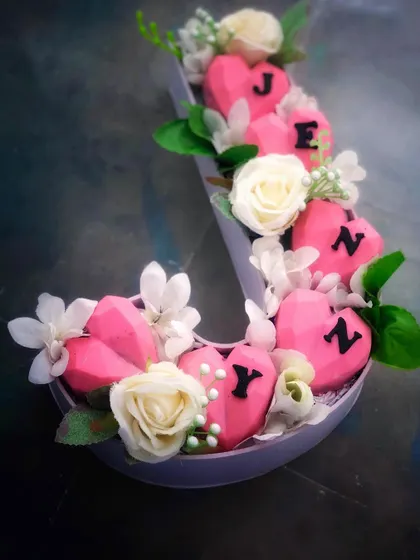 Pink heart-shaped monogram cakesicles sit among flowers in our personalised bouquet box, with letters across the small treats.