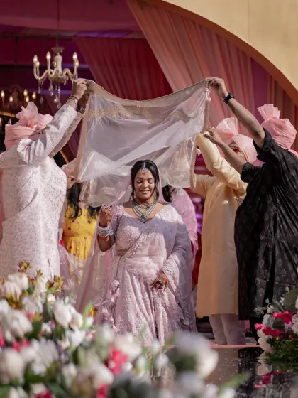 The bride's grand entrance. This photograph captures the beautiful tradition of the phoolon ki chadar, framing the bride as she walks towards the ceremony, surrounded by her loved ones.