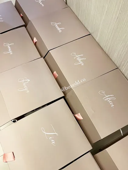 We handle bulk orders with a personal touch. Here is a set of bridesmaid gift boxes, each customized with the recipient's name, lined up and ready to be filled with curated goodies for the entire bride tribe.