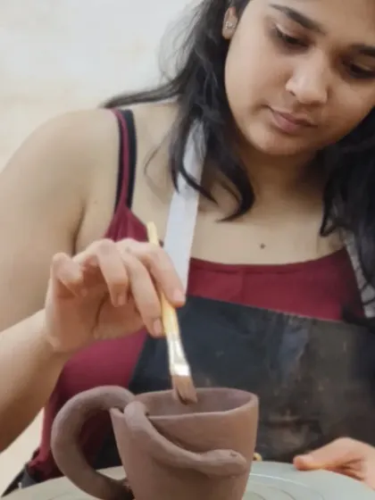 A student applies a finishing coat to her hand-built mug, which features a coiled snake as a handle. Our classes encourage imaginative designs and sculptural additions.