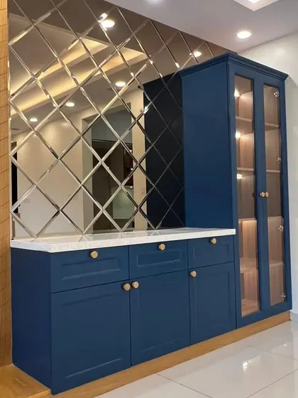 A stunning crockery unit in deep blue, featuring a glass-fronted display cabinet, drawers, and a countertop. The beveled mirror backsplash adds a luxurious and glamorous touch.