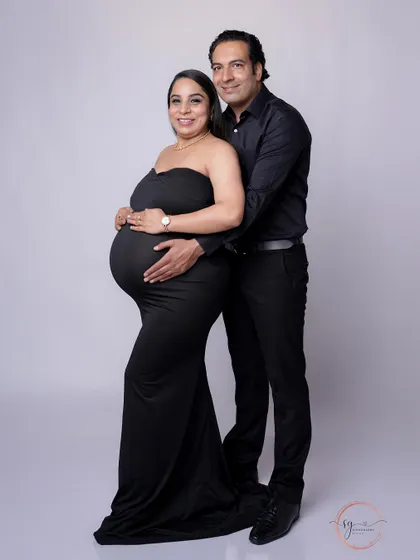 A full-length pose showing the couple's connection. The partner stands behind, embracing the mom-to-be in a protective and loving gesture.