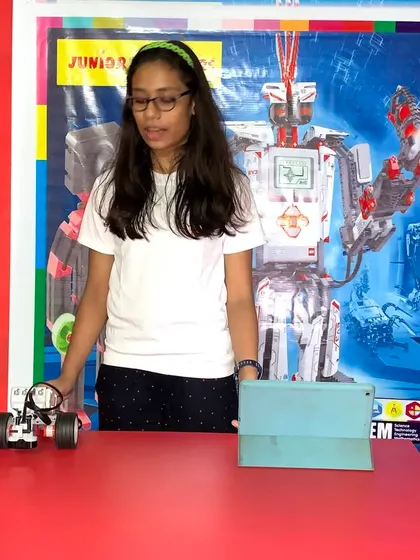A student presents her completed robot, ready for a challenge. The red classroom background is part of our stimulating learning environment, designed to inspire creativity.
