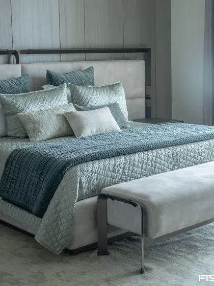 A serene bedroom in a luxurious penthouse. The custom bed features a metal frame and an upholstered headboard, paired with a matching bench. The cool blue and grey tones create a calming atmosphere.