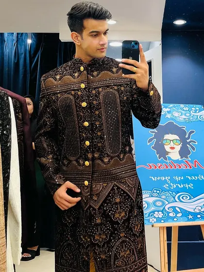 A mirror selfie of a client in a heavily embroidered brown and gold bandhgala, a rich and opulent choice for a wedding.