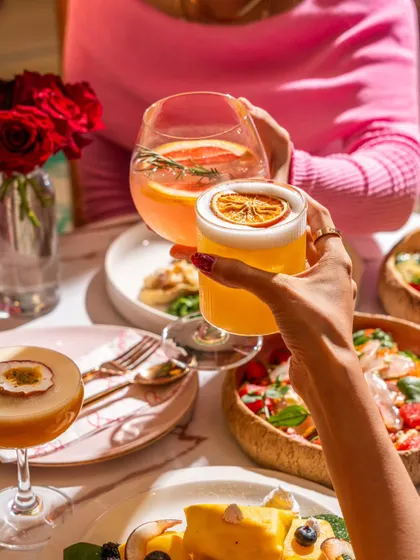 A "cheers" moment at Blah Bombay, with two hands clinking colorful cocktails. This classic lifestyle shot conveys celebration and social connection.