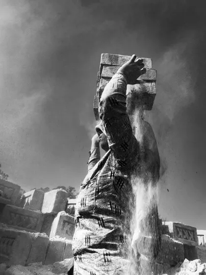 A dynamic black and white shot of a worker, with sand and dust cascading down as he works. The motion blur conveys a sense of constant activity.
