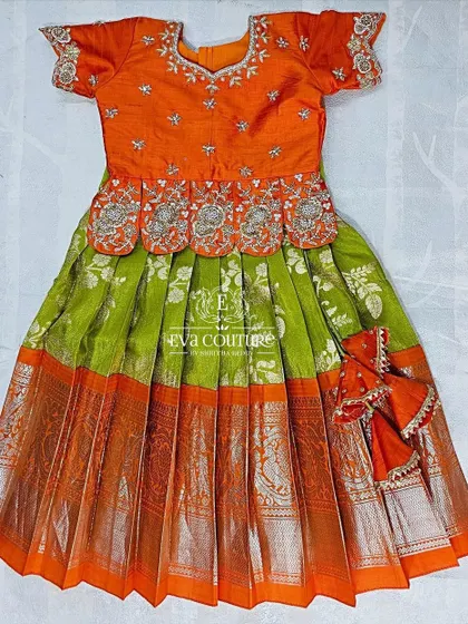 A ready-to-ship Kanchi pattu lehenga for a 6-month-old. The orange blouse has designer maggam work, and it's paired with a lime green skirt with a silver zari border.