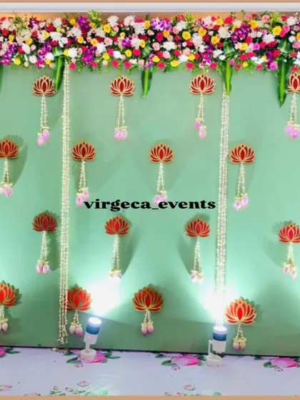 A lovely baby shower backdrop with a light green wall adorned with hanging lotus flowers and jasmine garlands.