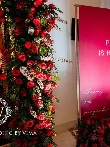 A bold and luxurious reception with a red and black color scheme. The decor includes rich red roses, modern crystal candelabras, and a stylish bar with a neon arch backdrop.