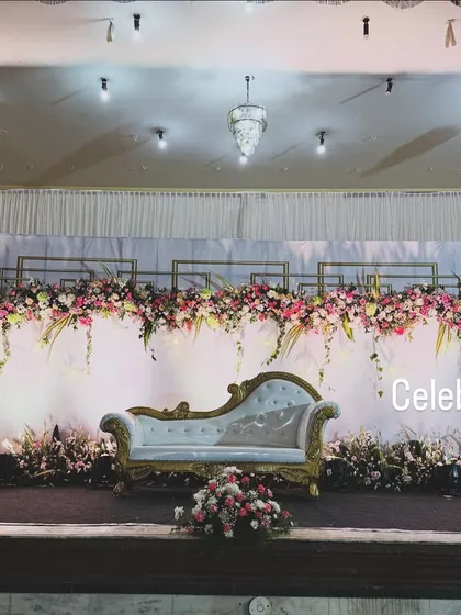 A clean and modern reception stage design. We used a white backdrop with geometric gold frames and lush floral arrangements for a sophisticated and chic look.