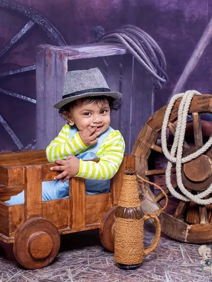 A cute cowboy moment in a rustic barn setting. The wooden cart, hay, and wagon wheel create a perfect backdrop for a little western adventure.