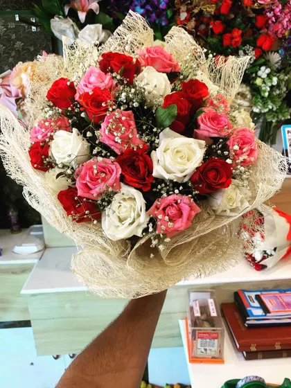 A beautiful bouquet of mixed red, pink, and white roses. The arrangement is wrapped in a natural jute net, giving it a rustic and organic feel.