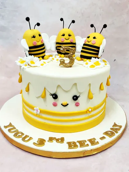 We create a buzz with this sweet-as-honey bumblebee theme cake. Three smiling bees sit atop a cake with dripping honey details and a cute face, making for an un-bee-lievably adorable "Bee-Day" celebration.