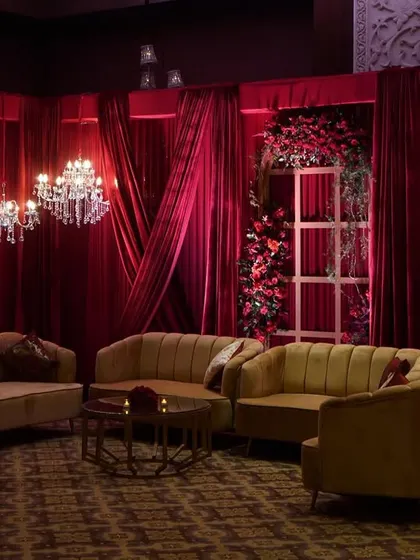 We create comfortable and stylish lounge areas for guests. This seating arrangement features plush mustard sofas set against a backdrop of red drapes, floral-adorned window frames, and elegant chandeliers.