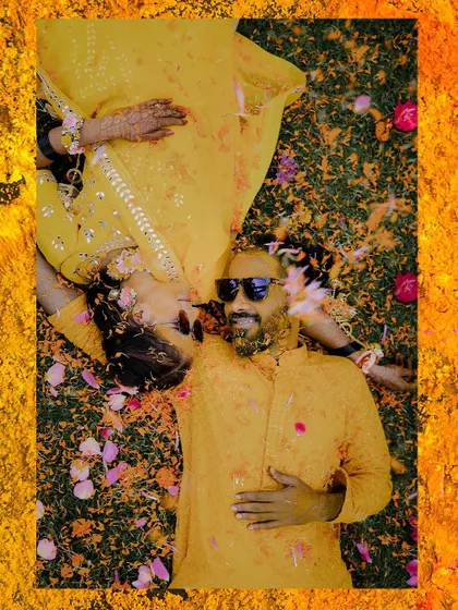 A creative top-down shot of the couple lying on a bed of flowers after their haldi.