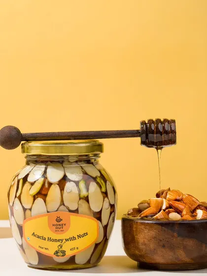 A jar of honey with nuts, with a honey dipper creating a perfect drip. This classic shot emphasizes the rich texture and quality of the honey.