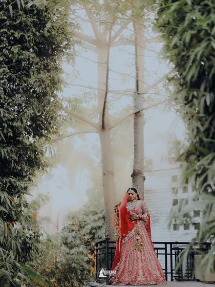 A wide-angle environmental portrait of bride Hashmeeta, framed by lush greenery, creating a serene and picturesque bridal shot.