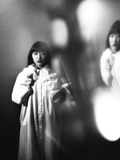 An experimental black and white film portrait using double exposure or a reflection. The ghostly second image adds a layer of psychological depth and visual complexity.