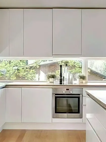 This bright and airy kitchen features all-white cabinetry and a light wood countertop. A long window above the sink floods the space with natural light, creating a pleasant cooking environment.