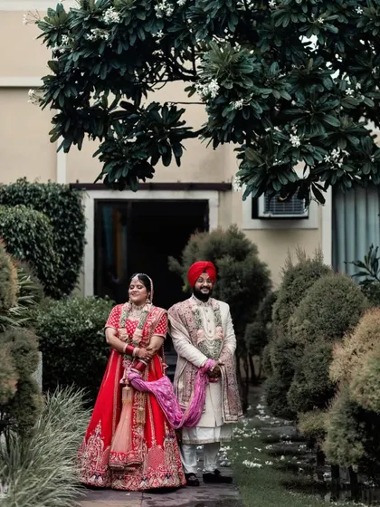 A wide shot of the couple in a garden setting. The framing by the tree above adds a natural, beautiful element to this timeless wedding portrait.