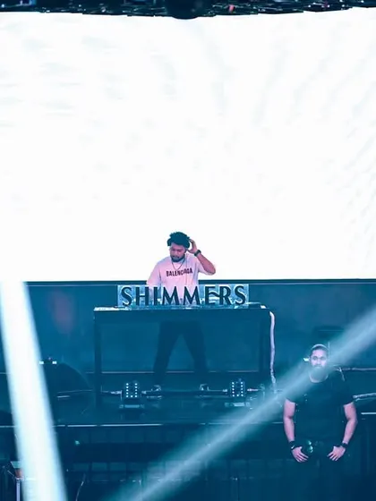A wide shot of me on the massive stage at Shimmers, with the bright white LED screen creating a powerful silhouette.