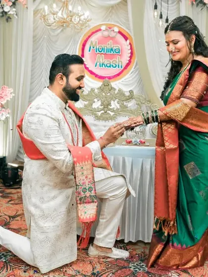 The groom-to-be gets down on one knee to place the ring on his fiancée's finger, a classic and heartwarming proposal moment during their engagement ceremony.