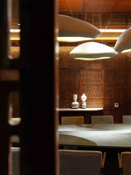 A detail shot of the dining room, seen through the intricate wooden lattice work. This view emphasizes the craftsmanship and the warm, filtered light that defines the space.