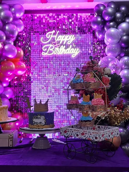 A closer view of the dessert table, highlighting the purple lighting on the sequin wall and the intricate details on the cakes and cupcakes.