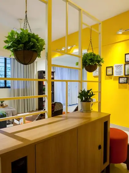 A bright and cheerful foyer with a vibrant yellow wall. The simple wooden console and metal frame partition with hanging plants create a fresh and modern look.
