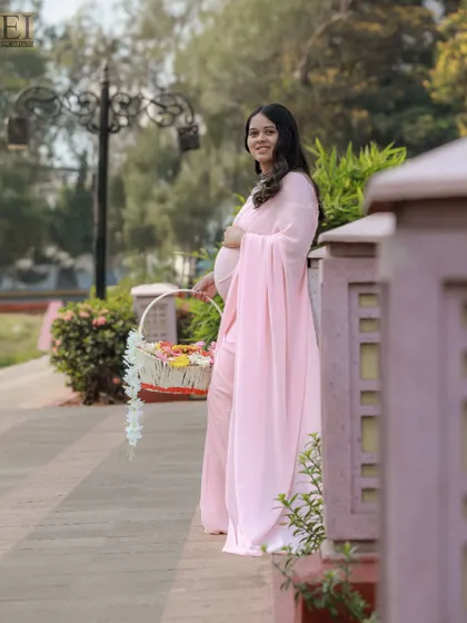A candid, smiling portrait of the mom-to-be in her pink saree, captured in a natural outdoor setting.