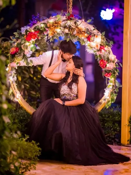 A romantic moment captured on a floral swing. The black ball gown and the partner's classic white shirt with suspenders create a timeless and elegant couple's portrait.