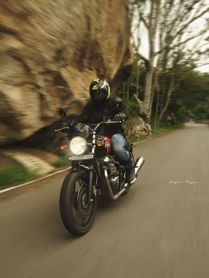 A rider on a Royal Enfield motorcycle navigates a winding road, with the motion blur giving a great sense of speed. This panning shot captures the thrill of riding through a scenic route.