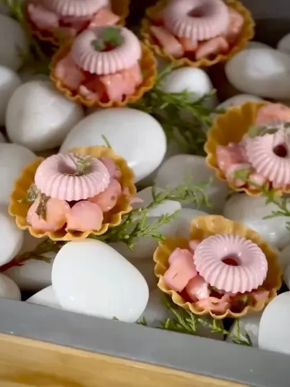 A beautiful canapé featuring a pink mousse in a crisp tart shell, presented on a bed of white pebbles.